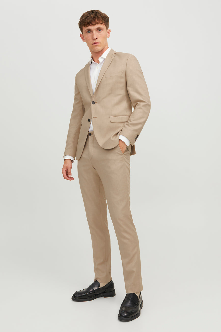 Pantalon de costume beige par PREMIUM BY JACK & JONES, coupe ajustée, porté avec veste assortie et chaussures noires.
