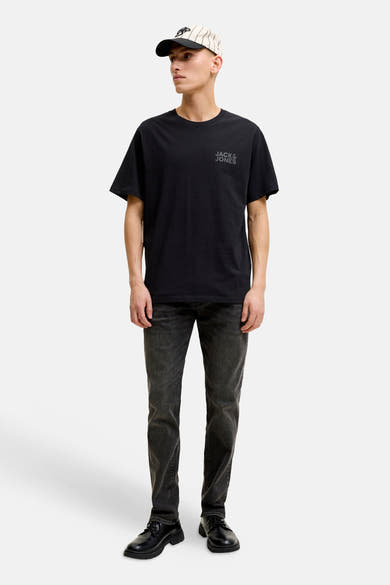 Zwart T-shirt met korte mouwen van JACK & JONES met discreet grijs logo, gedragen door een man met een lichtgrijze jeans en een gestreepte pet.