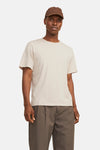 T-shirt beige à manches courtes de JACK & JONES, porté avec un pantalon marron plissé et une casquette.
