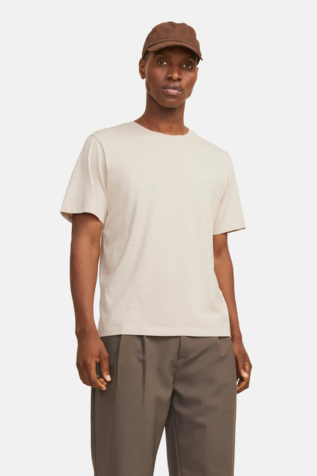 Beige T-shirt met korte mouwen van JACK & JONES, gedragen met een bruine plooibroek en een pet.
