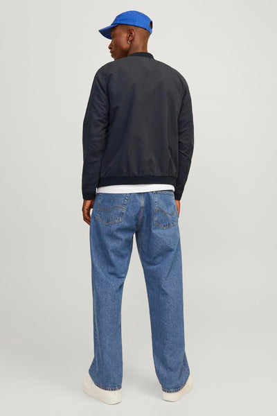 Veste courte noire de PREMIUM BLUE BY JACK & JONES, avec fermeture éclair, portée avec un t-shirt blanc, un jean bleu et des baskets blanches.