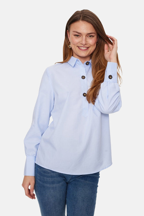 Blouse bleu à manches longues de FREEQUENT, avec boutons marron sur le devant et aux poignets, portée avec un jean.
