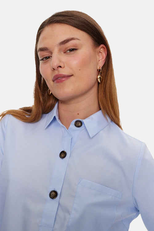 Blouse à manches longues bleue de Freequent, avec col chemise, boutons marron foncé et poche de poitrine.