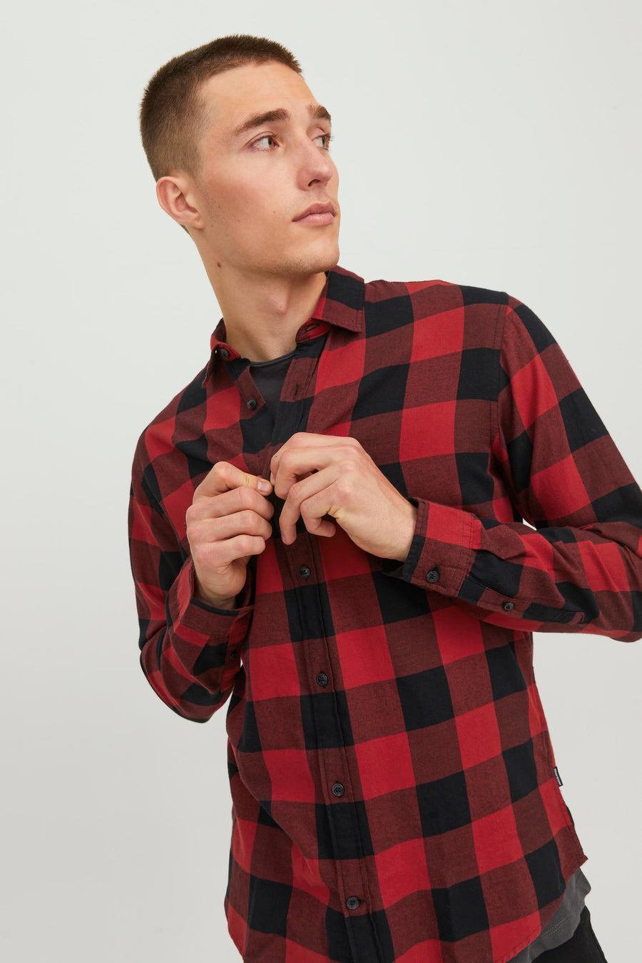 Rood geruit overhemd met lange mouwen van JACK & JONES, gedragen door een man die zijn overhemd dichtknoopt.