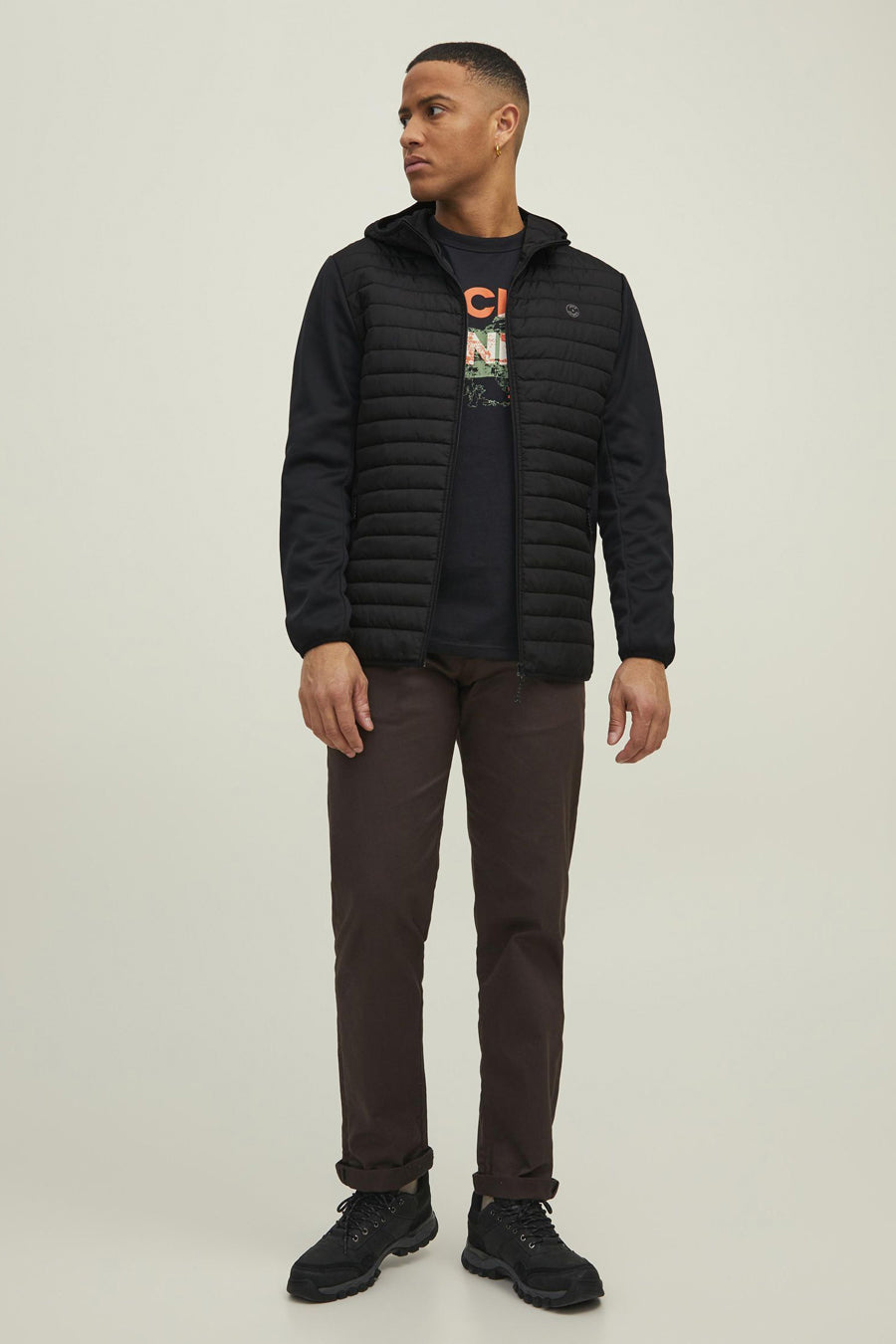 Zwarte waterdichte jas van JACK & JONES, met capuchon, gedragen door een man met een T-shirt en een bruine broek.