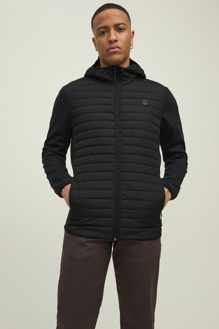 Veste noire par JACK & JONES, matelassée avec capuche et manches longues en tissu lisse, portée avec un pantalon marron.