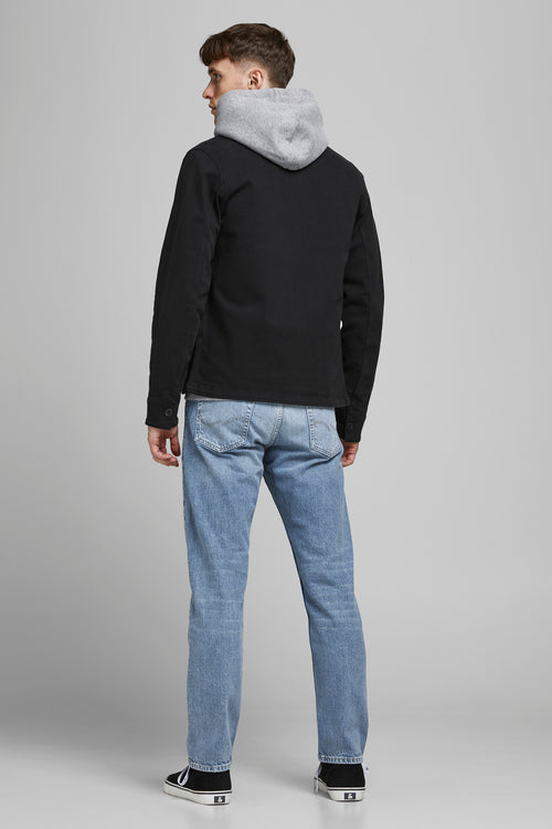 Jeans fuselé bleu clair denim de JACK & JONES JEANS INTELLIGENCE, porté par un homme de dos avec une veste noire et des baskets.
