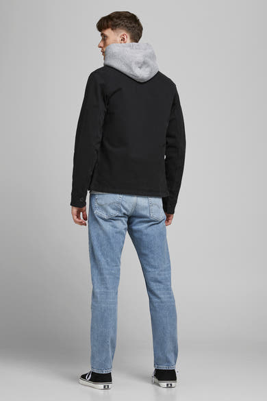 Jeans fuselé bleu clair denim de JACK & JONES JEANS INTELLIGENCE, porté par un homme de dos avec une veste noire et des baskets.