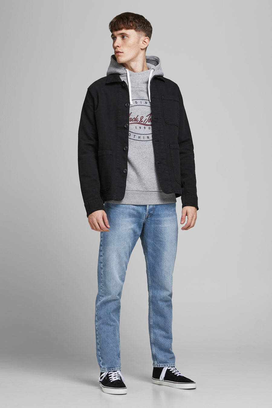 Jeans tapered bleu clair de JACK & JONES JEANS INTELLIGENCE, portés par un homme avec un hoodie gris et une surchemise noire.
