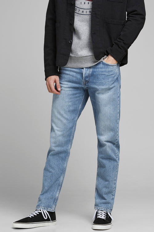 Jeans tapered en denim bleu clair de JACK & JONES JEANS INTELLIGENCE, portés avec des baskets et une veste noire.