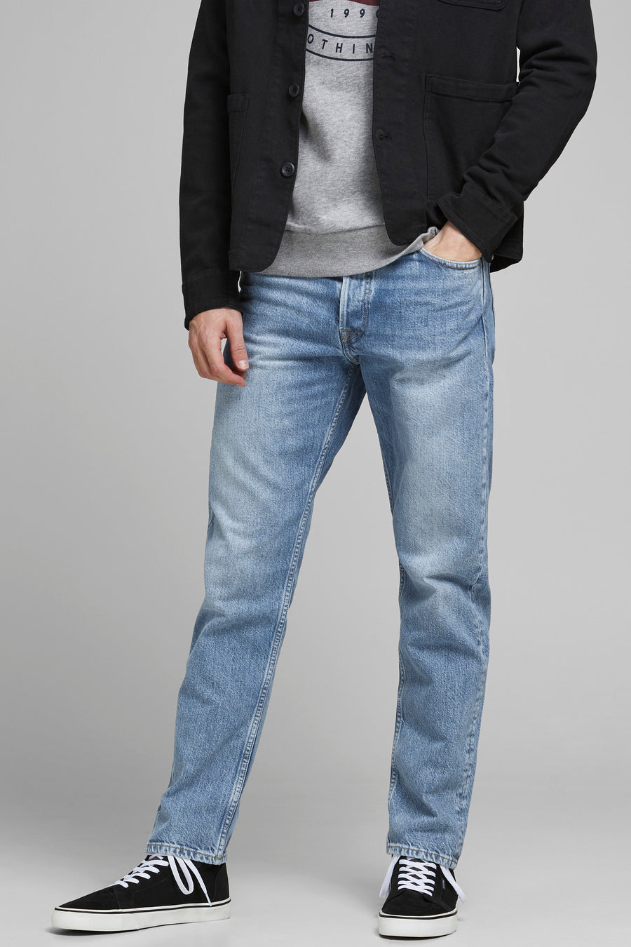 Jeans tapered en denim bleu clair de JACK & JONES JEANS INTELLIGENCE, portés avec des baskets et une veste noire.