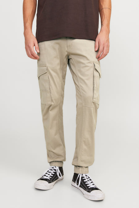 Pantalon cargo beige de JACK & JONES JEANS INTELLIGENCE avec poches et ourlets élastiqués, porté avec un t-shirt marron et des baskets noires.