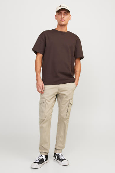 Pantalon cargo beige de JACK & JONES JEANS INTELLIGENCE, porté avec un t-shirt marron, des baskets noires et une casquette.
