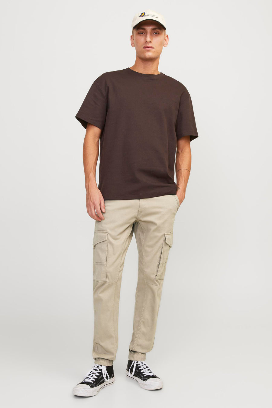 Pantalon cargo beige de JACK & JONES JEANS INTELLIGENCE, porté avec un t-shirt marron, des baskets noires et une casquette.
