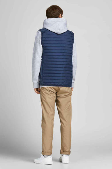 Blauwe mouwloze jas van JACK & JONES, gedragen over een grijze hoodie en een beige chino broek.