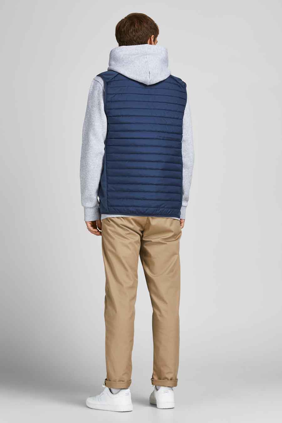 Blauwe mouwloze jas van JACK & JONES, gedragen over een grijze hoodie en een beige chino broek.