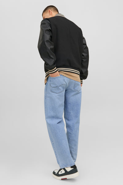Jean large bleu moyen de JACK & JONES JEANS INTELLIGENCE, porté avec une veste universitaire noire et des chaussures de sport.