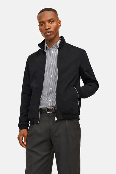 Veste courte noire JACK & JONES avec fermeture éclair, portée sur une chemise rayée et un pantalon noir.