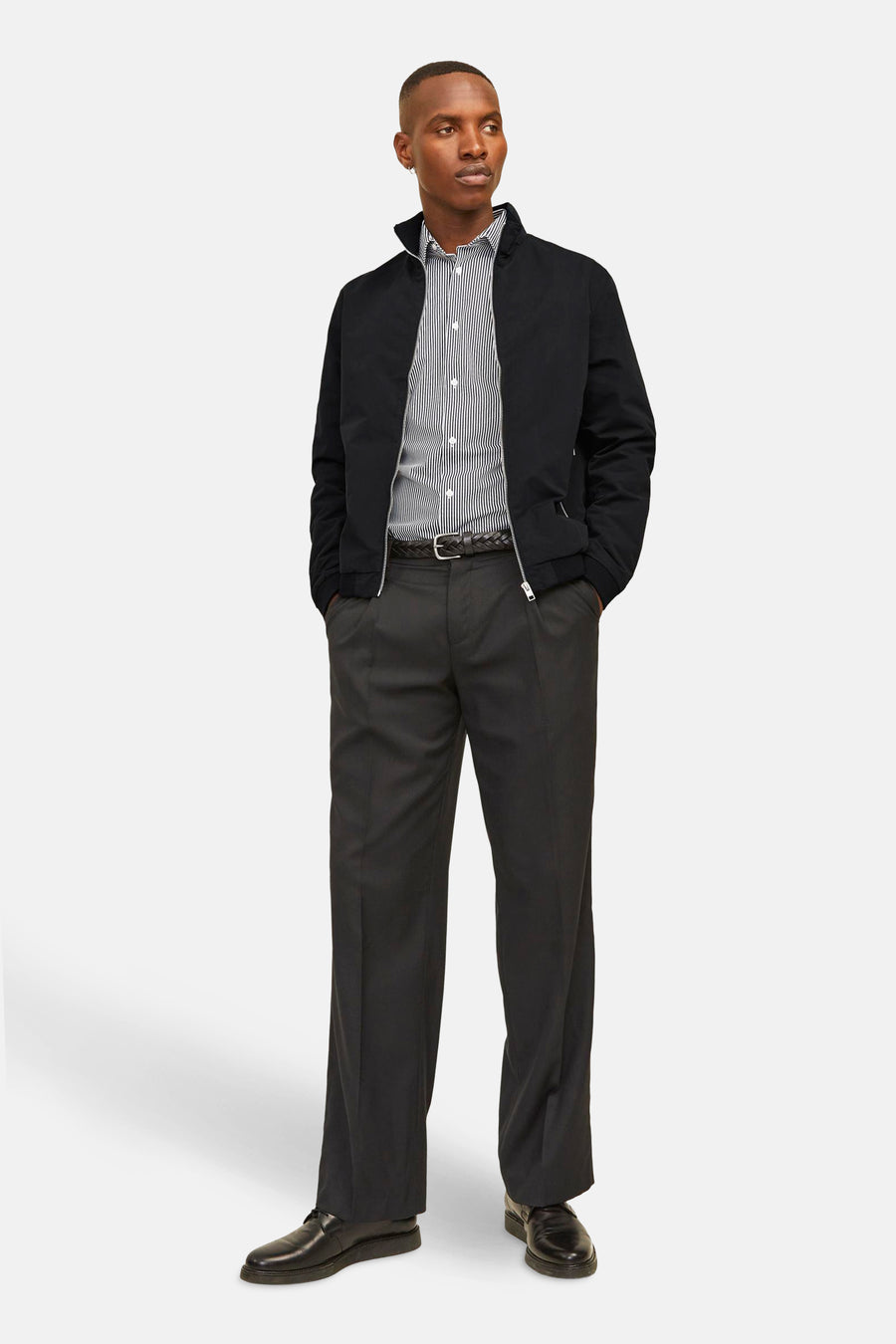 Veste courte noire de JACK & JONES, portée sur une chemise rayée et un pantalon sombre, poches apparentes.
