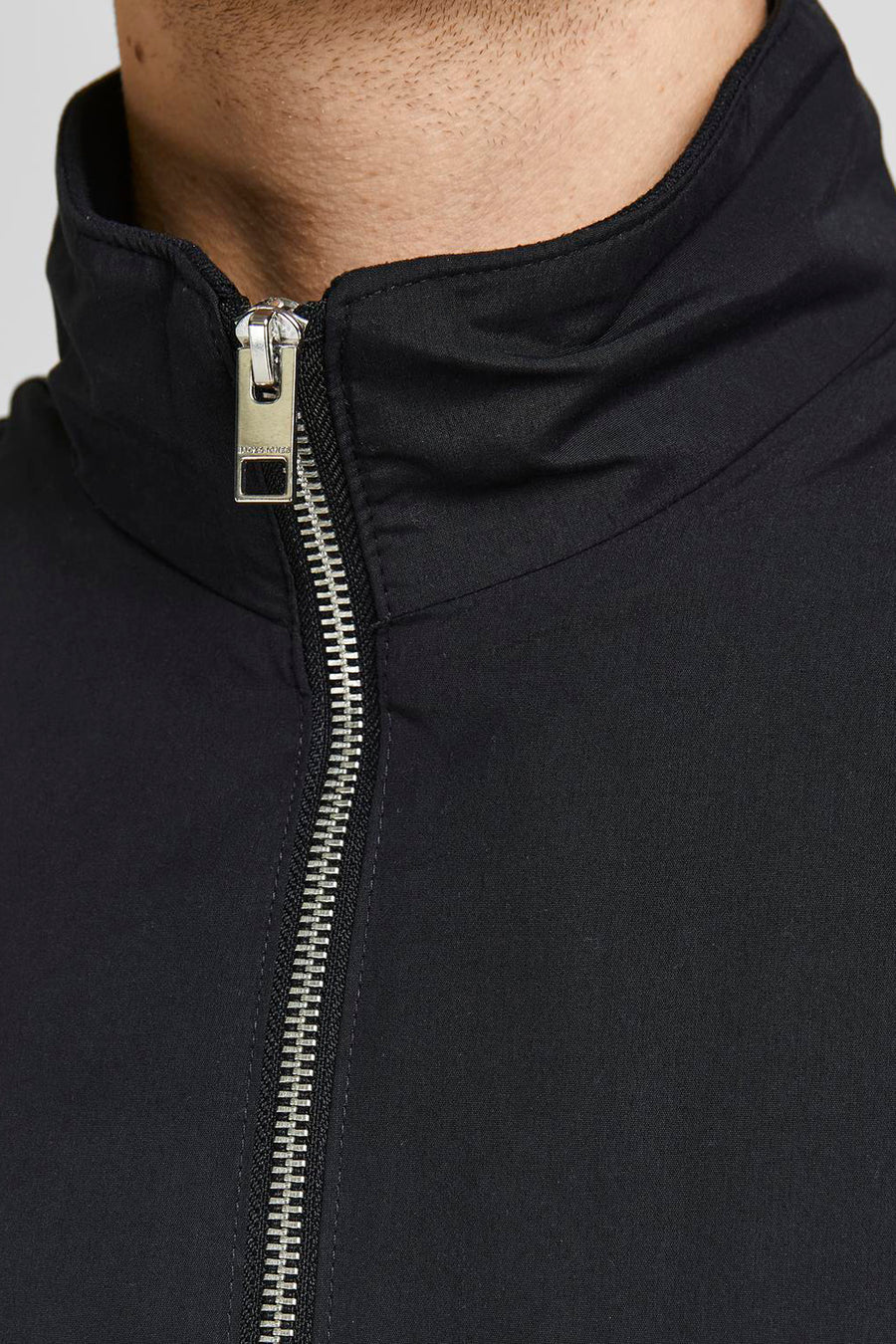 Korte zwarte jas van JACK & JONES met een zilveren ritssluiting aan de voorkant.