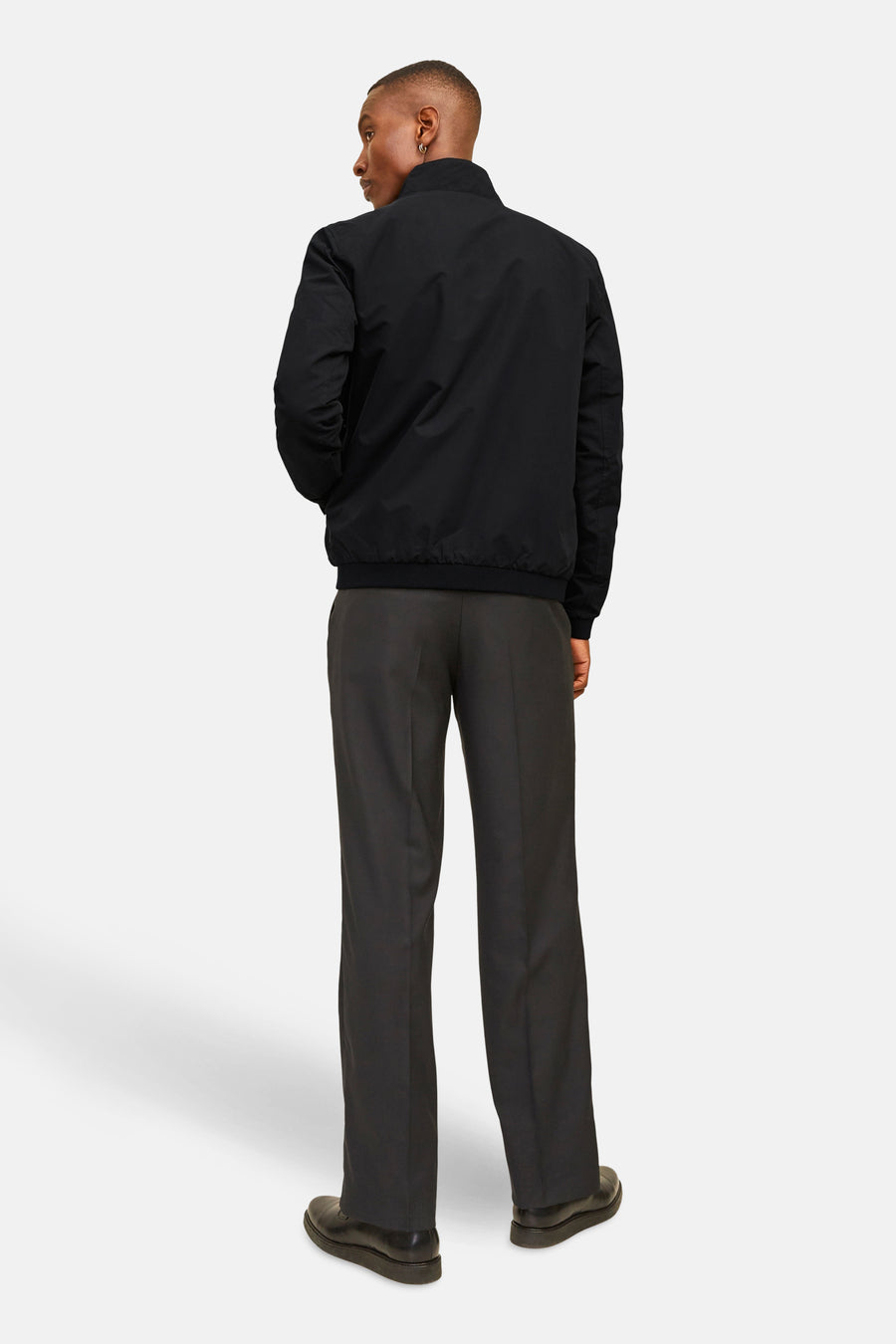 Veste courte noire de JACK & JONES, vue de dos, portée avec un pantalon de costume gris et des chaussures noires.