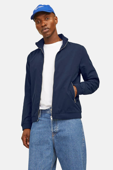 Korte blauwe jas van JACK & JONES, met ritssluiting, gedragen met een wit T-shirt en een blauwe hoed.