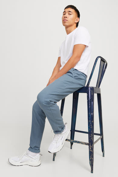 Chino bleu de JACK & JONES, porté avec un t-shirt blanc et des baskets blanches sur un tabouret bleu.
