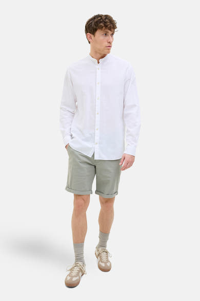 Korte olijfgroene short JACK & JONES JEANS INTELLIGENCE, gedragen met een wit overhemd met lange mouwen en beige sneakers.