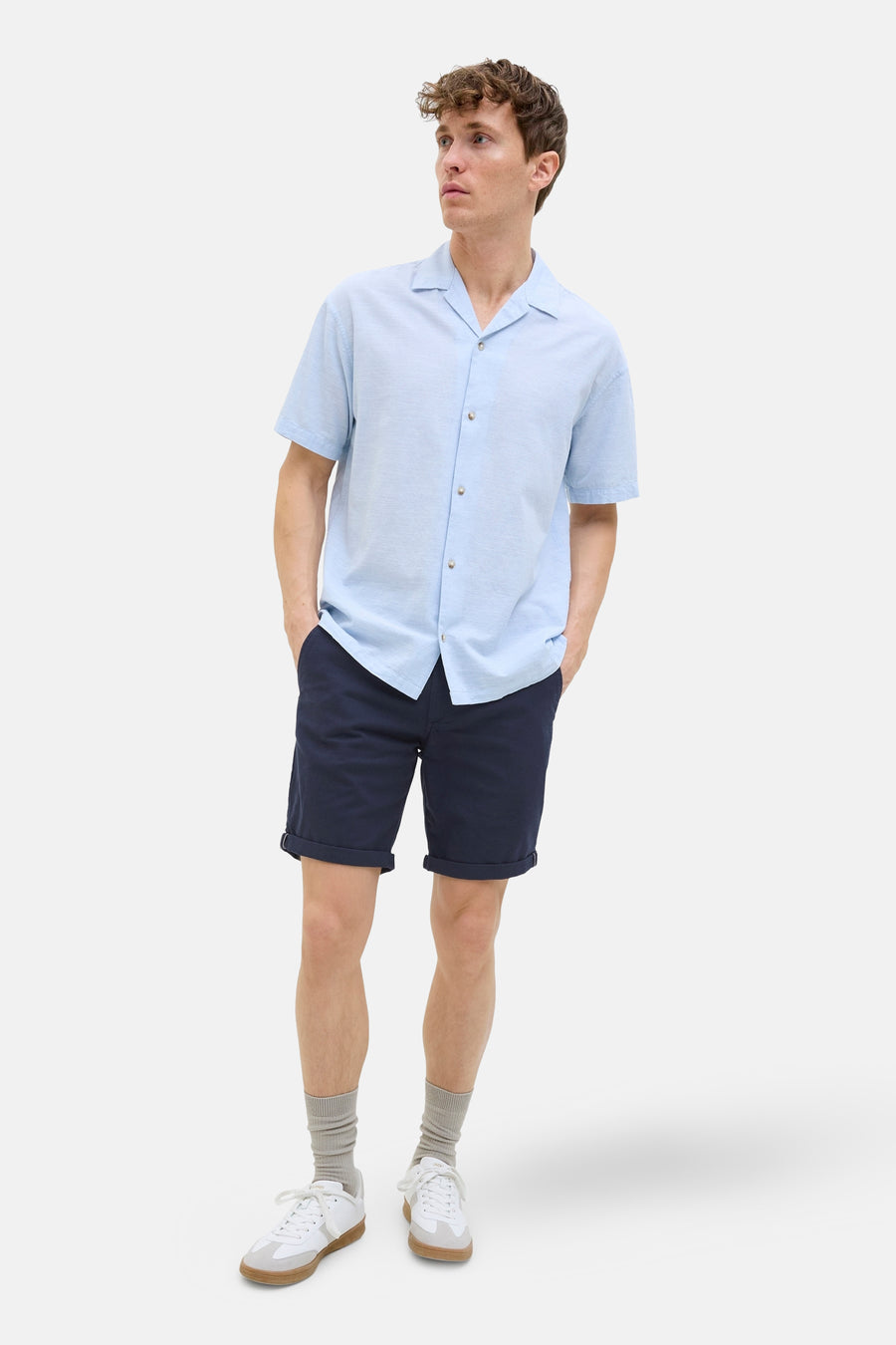 Korte blauwe short van JACK & JONES JEANS INTELLIGENCE, met omgeslagen zomen, gedragen met lichtblauw overhemd, grijze sokken en witte sneakers.