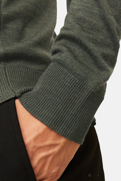 Khaki ronde hals trui van PREMIUM by JACK & JONES, geribbelde gebreide details op de manchet en hand in de zak van de zwarte broek.