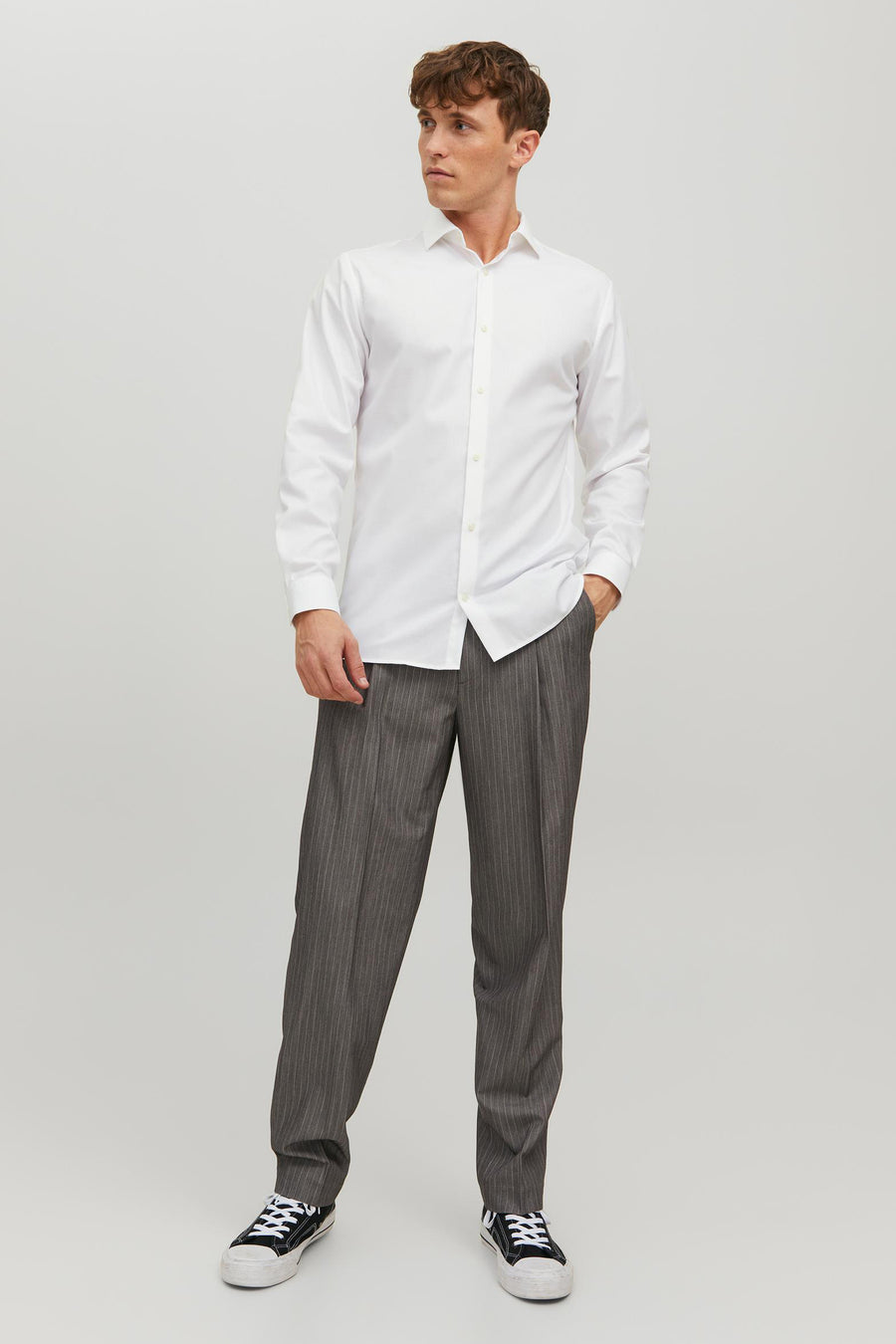 Wit overhemd met lange mouwen van PREMIUM by JACK & JONES, gedragen met een gestreepte broek en sneakers.