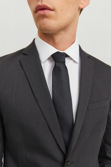 Cravate noire de ACCESSORIES BY JACK & JONES, portée avec une chemise blanche et un costume gris anthracite.