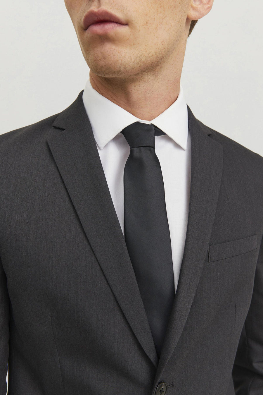 Cravate noire de ACCESSORIES BY JACK & JONES sur une chemise blanche et un costume gris foncé.