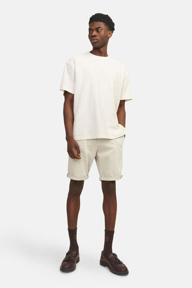 Short beige JACK & JONES JEANS INTELLIGENCE, à motifs discrets, porté avec un t-shirt écru, des chaussettes marron et des mocassins.
