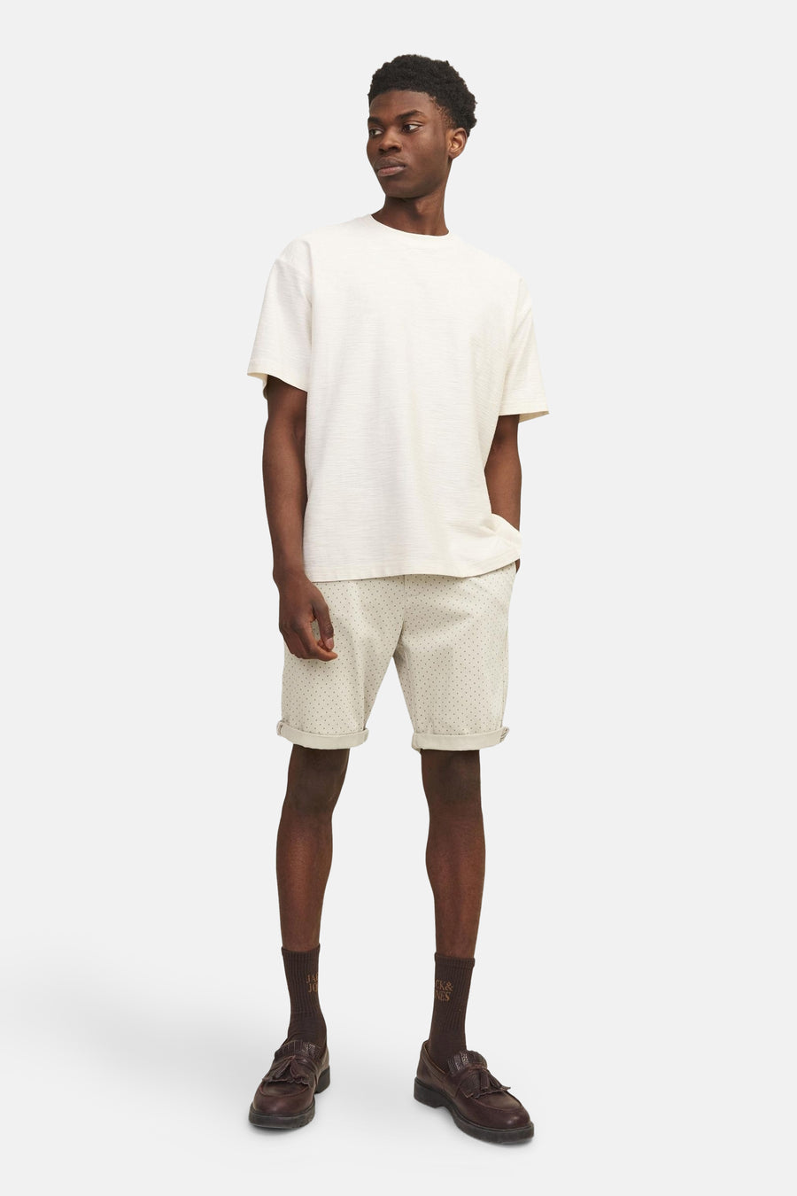Short beige JACK & JONES JEANS INTELLIGENCE, à motifs discrets, porté avec un t-shirt écru, des chaussettes marron et des mocassins.
