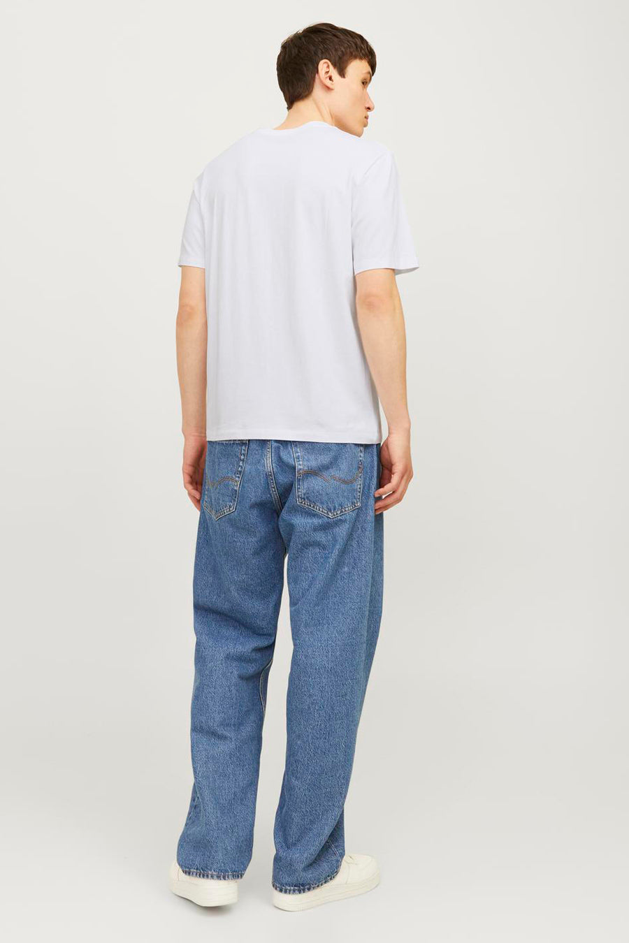 Wit T-shirt met korte mouwen van JACK & JONES, gedragen met een wijde blauwe jeans en witte sneakers, achtergezicht.