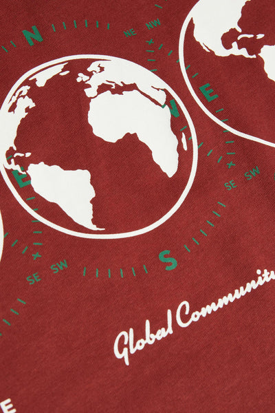 Red short-sleeve t-shirt with white globe print and green compass details, featuring "Global Community" text, close-up view