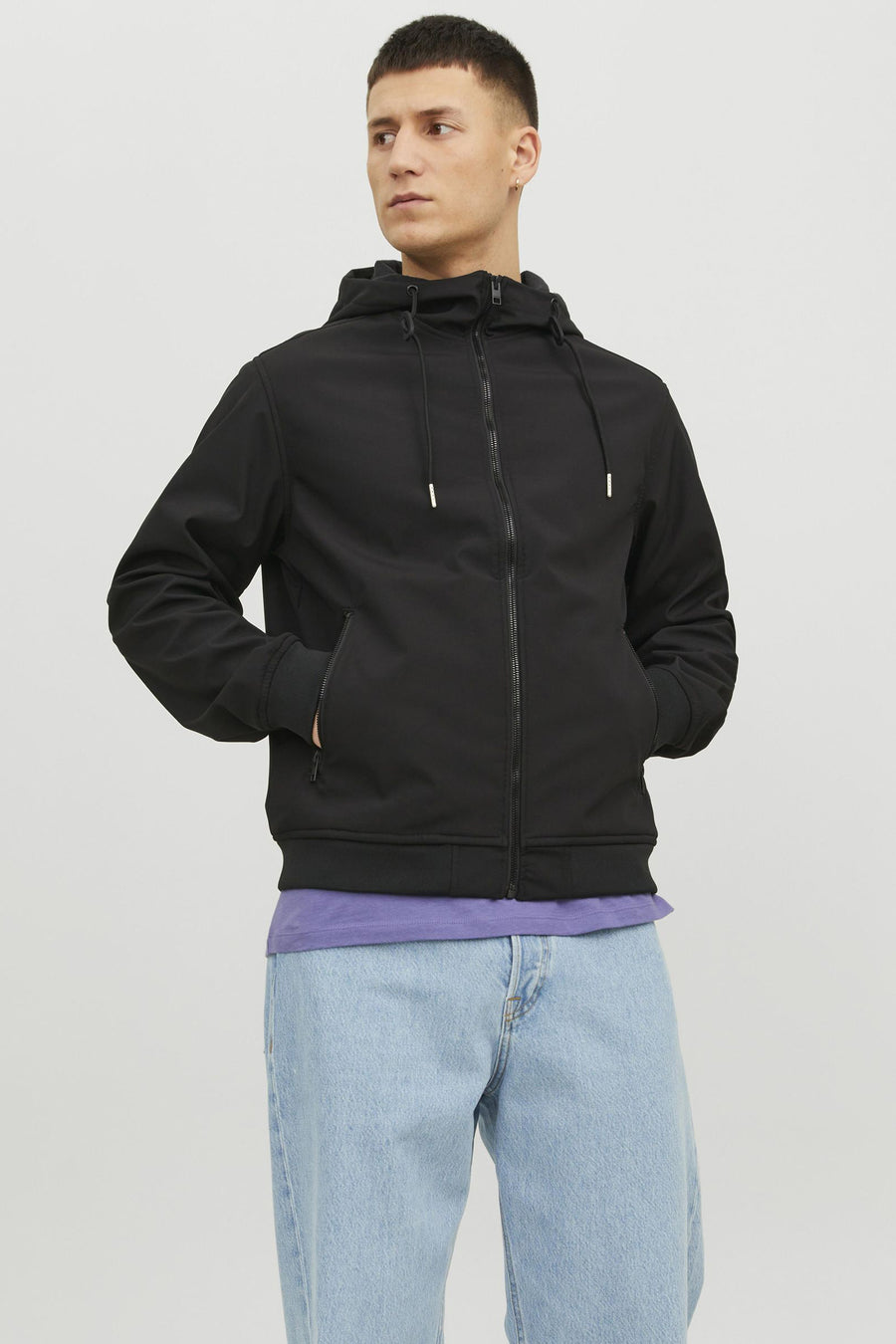 Veste courte noire de JACK & JONES, avec capuche et poches avant, portée avec un t-shirt violet et un jean bleu.