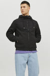 Veste courte noire de JACK & JONES avec capuche, poches zippées et manches longues, portée sur un t-shirt violet et un jean bleu clair.