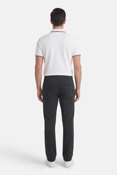 Chino noir de JACK & JONES JEANS INTELLIGENCE avec poches arrière passepoilées, porté avec un polo blanc à rayures.