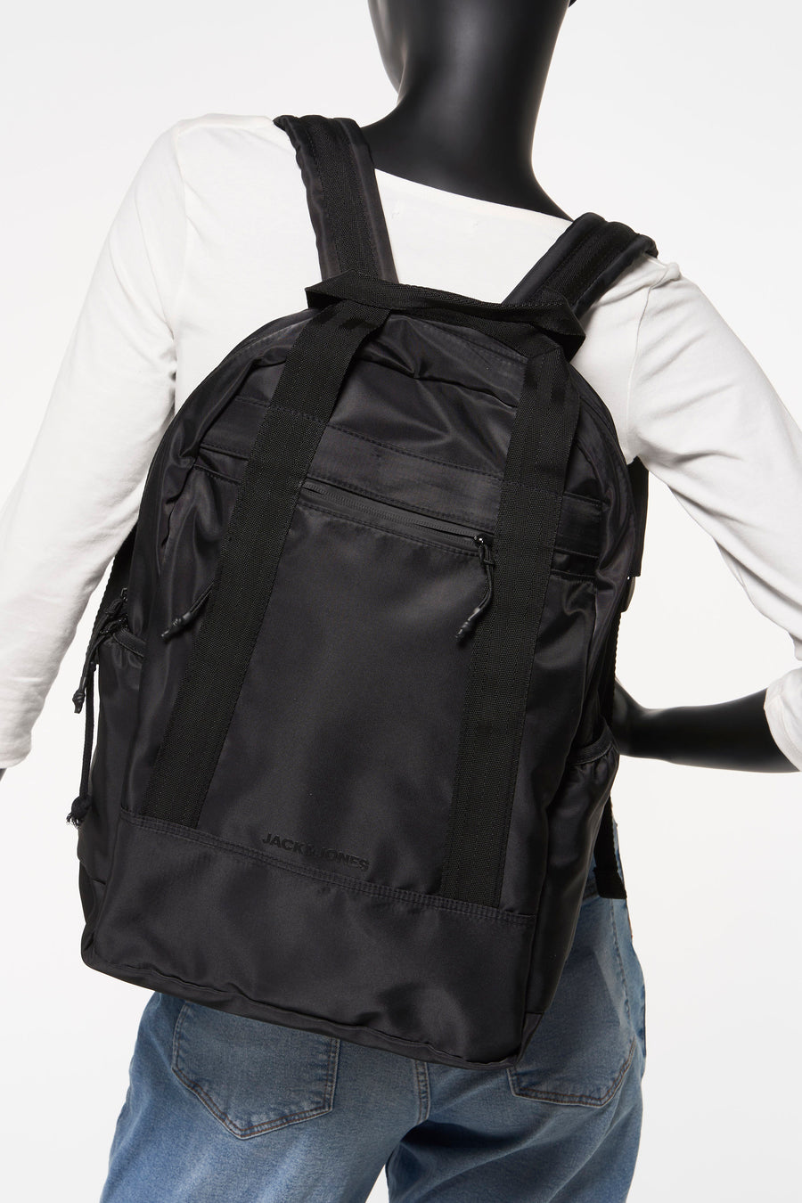 Zwarte rugzak van ACCESSORIES BY JACK & JONES, gedragen door een model met een witte trui en een blauwe jeans.