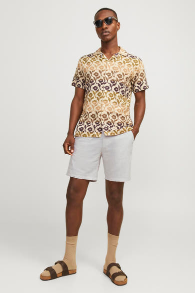 Short beige de JACK & JONES JEANS INTELLIGENCE, porté avec une chemise à fleurs, des chaussettes beige et des sandales.
