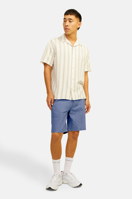 Korte blauwe jeans van JACK & JONES JEANS INTELLIGENCE, gedragen met een gestreept overhemd, witte sokken en witte sneakers.