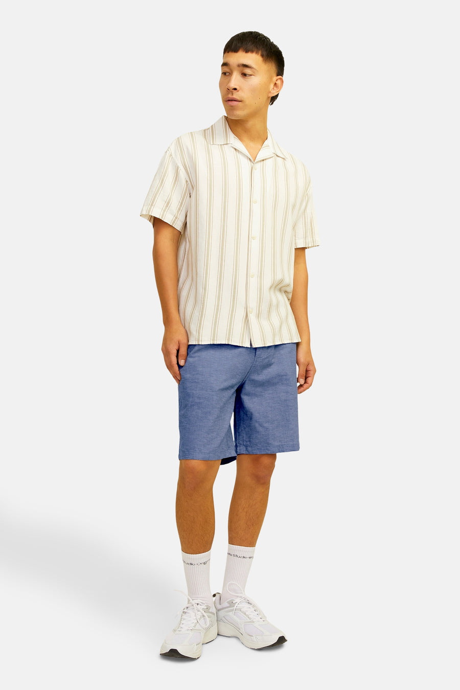 Short bleu de JACK & JONES JEANS INTELLIGENCE, porté avec une chemise rayée, des chaussettes blanches et des baskets blanches.