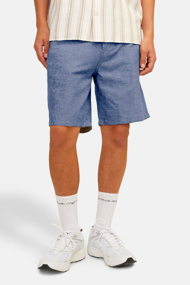 Short bleu de JACK & JONES JEANS INTELLIGENCE, porté avec une chemise rayée et des baskets blanches.