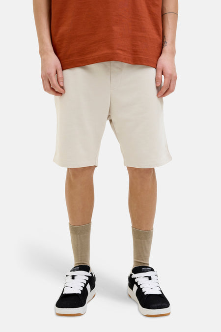 Korte ecru short van JACK & JONES JEANS INTELLIGENCE van fleece, gedragen met een roestkleurig T-shirt en sneakers.