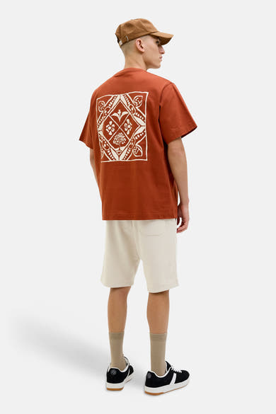 Korte ecru joggingbroek van fleece van JACK & JONES JEANS INTELLIGENCE, van achteren gezien, gedragen met een T-shirt met print en een pet.