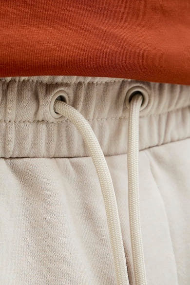 Kort ecru short van JACK & JONES JEANS INTELLIGENCE met beige gevlochten trekkoord en oogjes, op een oranje mesh stof.