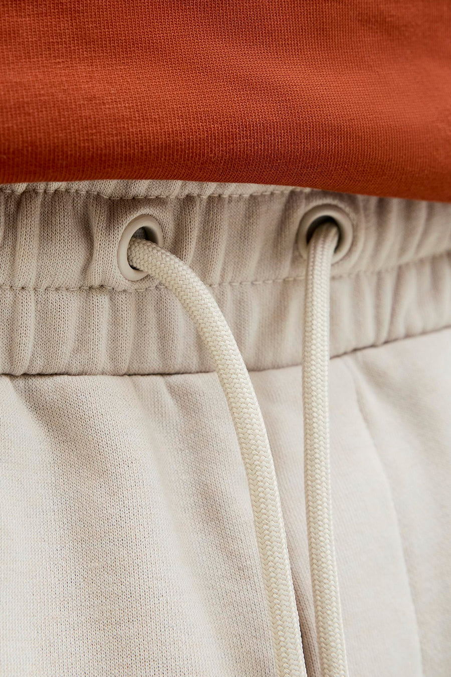 Kort ecru short van JACK & JONES JEANS INTELLIGENCE met beige gevlochten trekkoord en oogjes, op een oranje mesh stof.
