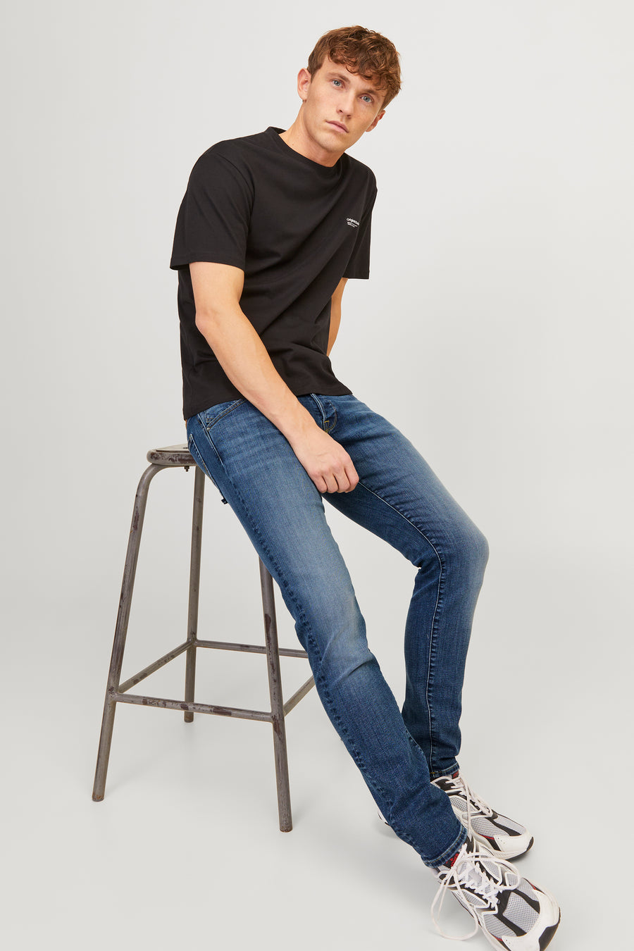 Middelblauwe slim fit jeans van JACK & JONES JEANS INTELLIGENCE gedragen met een effen zwart T-shirt en witte sneakers.